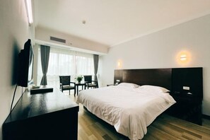 Habitación de hotel con cama, escritorio, silla, televisor y ventana con cortinas.