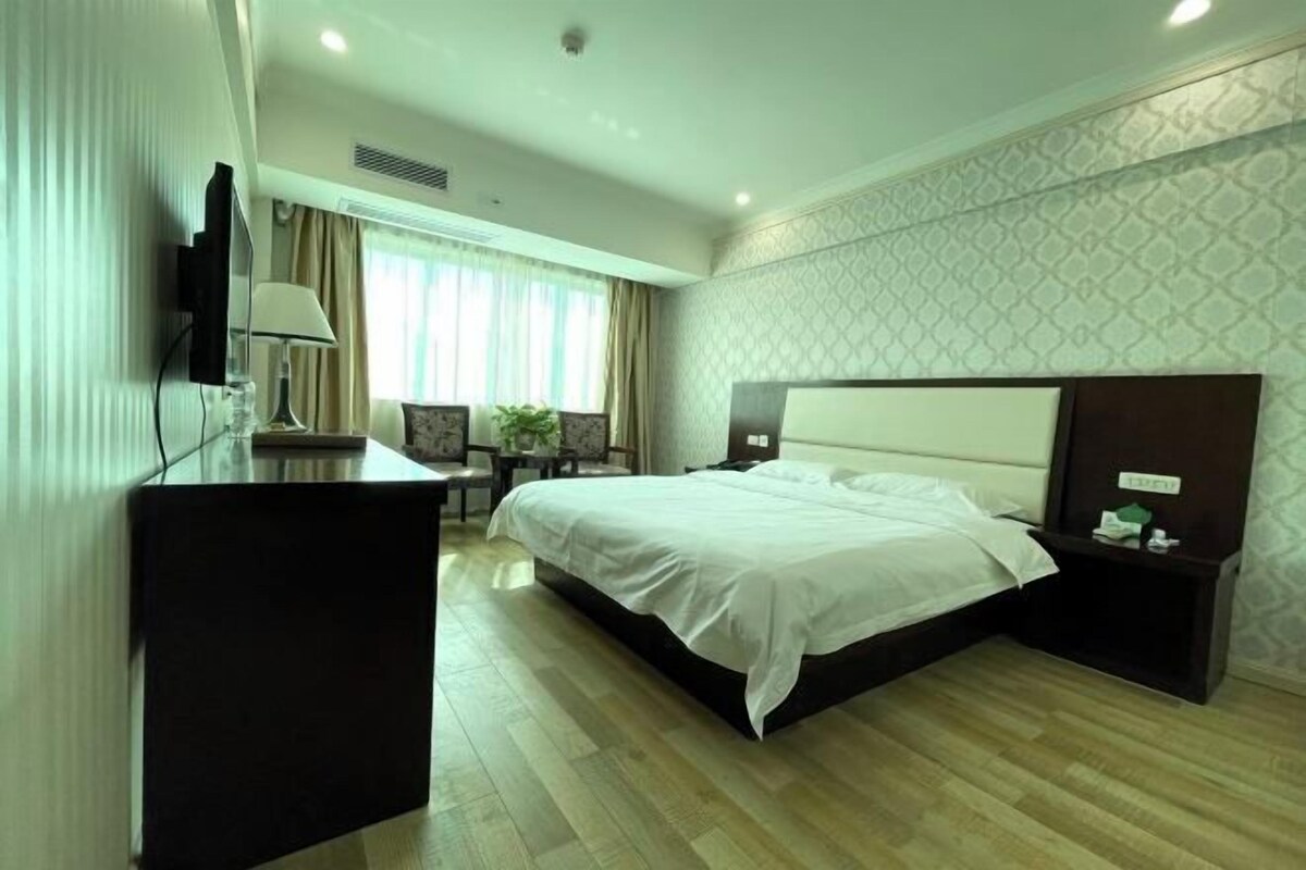 Una habitación de hotel con cama, mesita de noche, lámpara, televisión y un escritorio con silla.