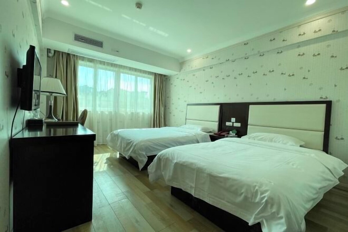 Habitación de hotel con dos camas, un escritorio, un televisor y una ventana con cortinas.