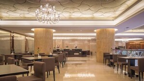 Un amplio hall de hotel con una lámpara de araña moderna, una recepción y varias mesas y sillas para comer.