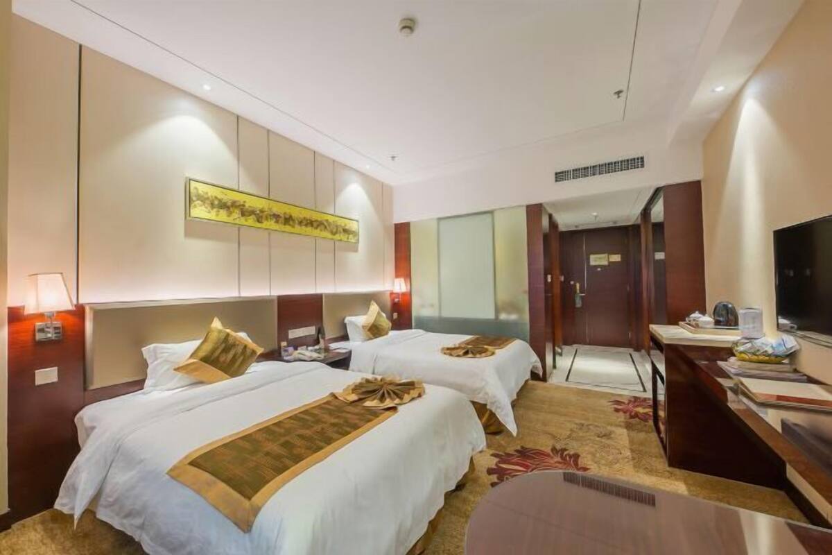 A hotel room with two beds, a desk, a TV, and a large artwork on the wall.