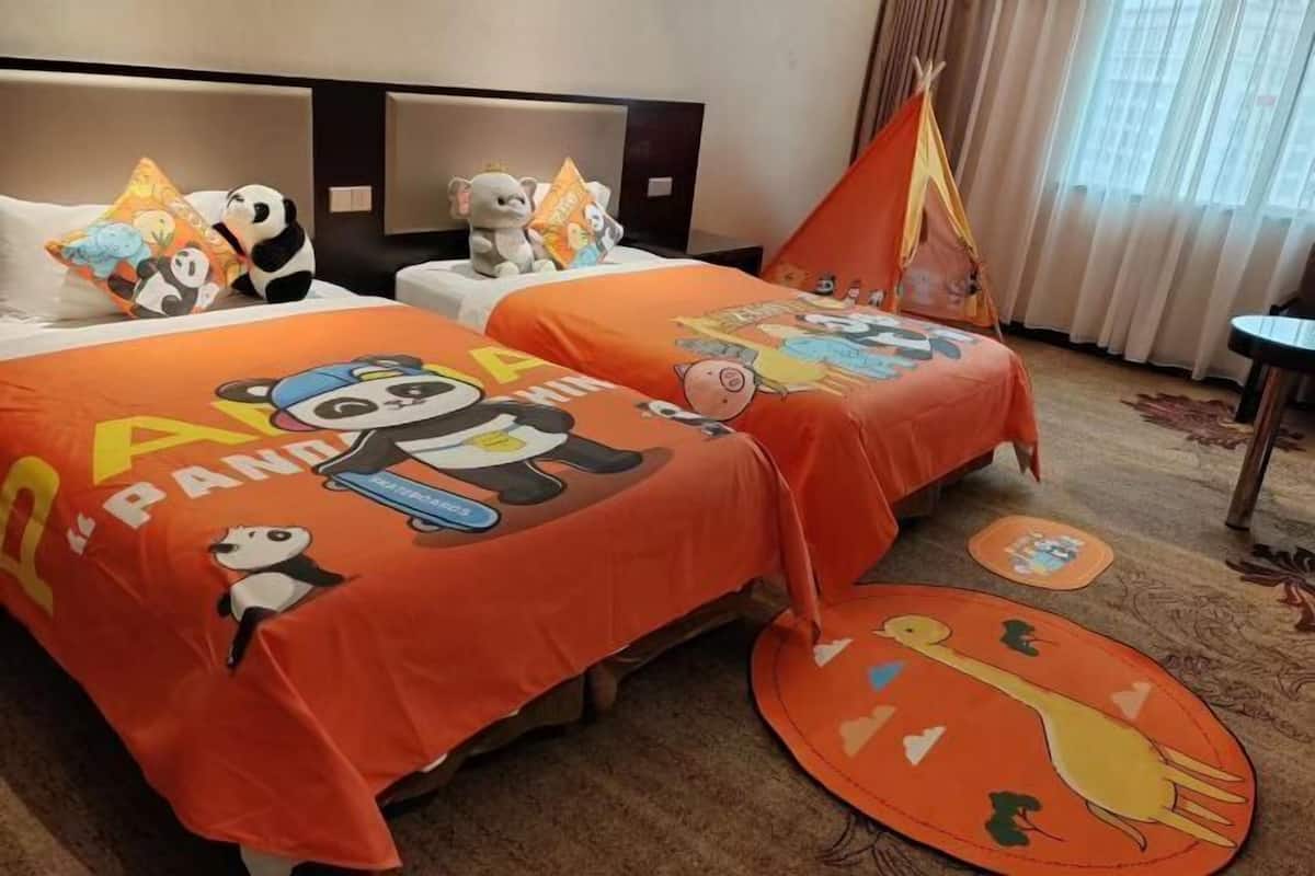 A hotel room with two beds, each covered with panda-themed bedding. There is a small table and a chair, and a decorative teepee in the corner.