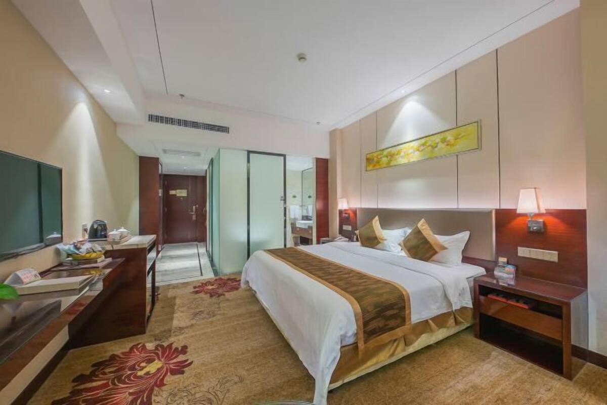 A hotel room with a bed, bedside table, lamp, and a desk with a chair.