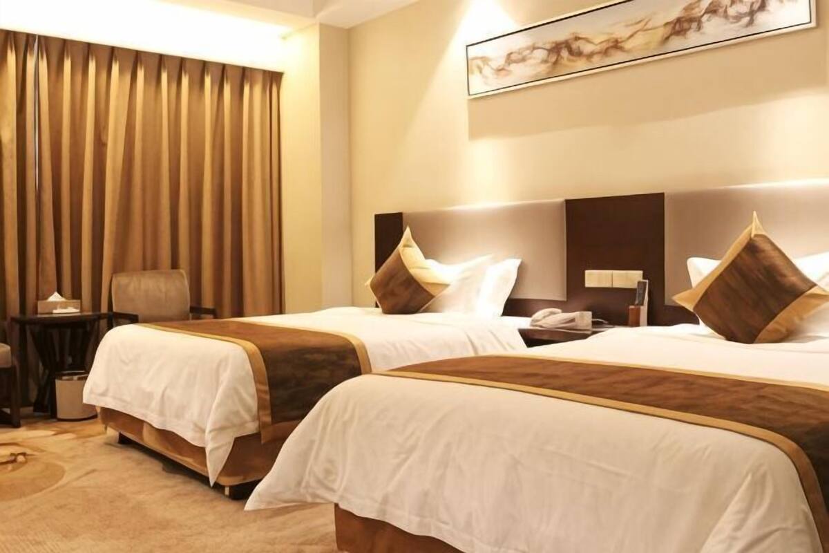 A hotel room with two beds, a desk, a chair, and a large window with curtains.