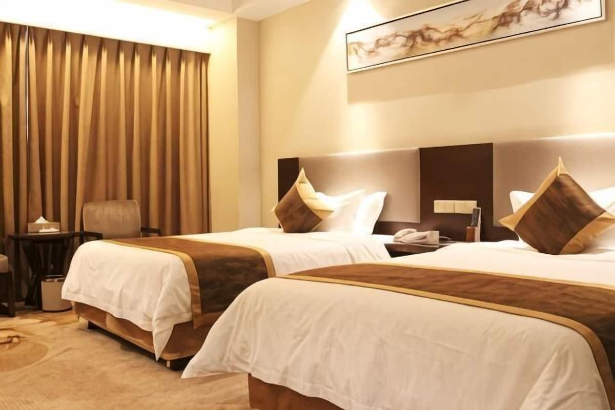 A hotel room with two beds, a desk, a chair, and a large window with curtains.