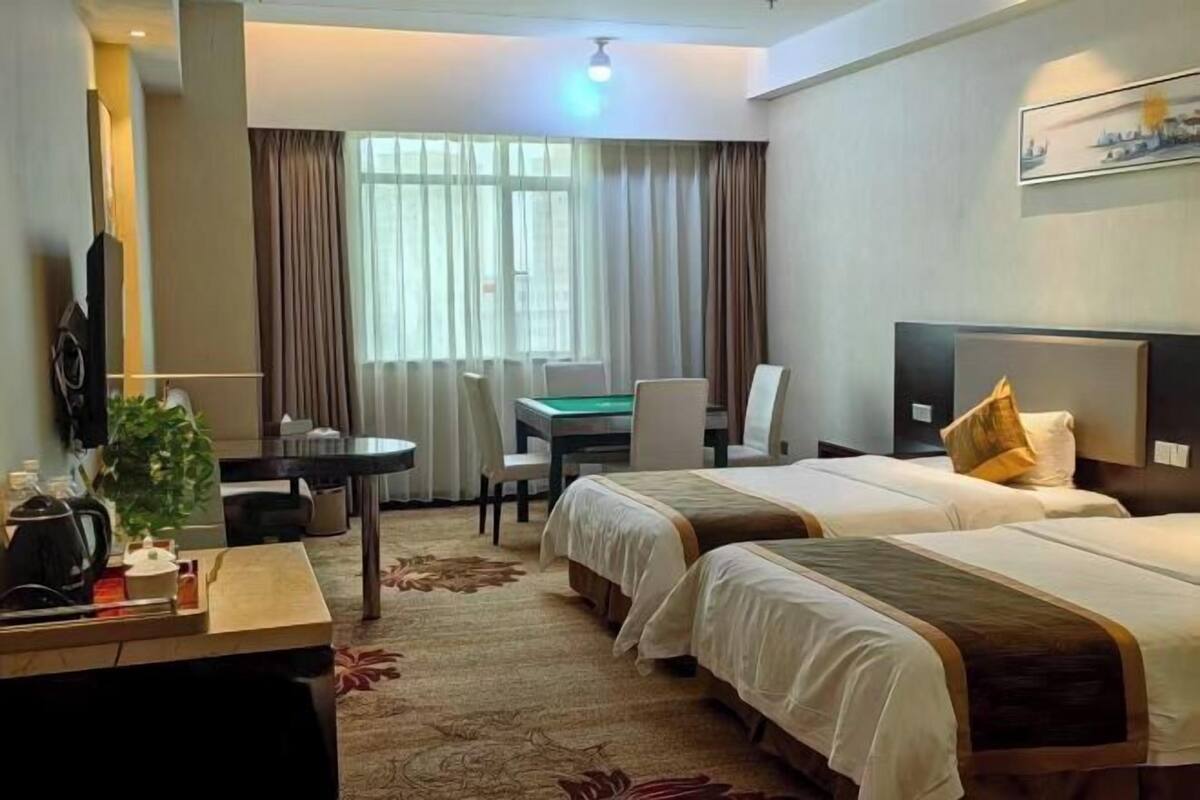 A hotel room with two beds, a desk, a chair, a TV, and a window with curtains.