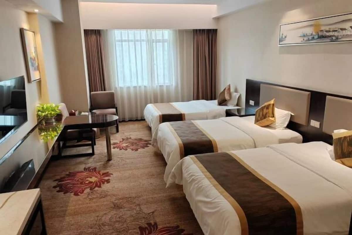 A hotel room with two beds, a desk, a TV, and a window with curtains.