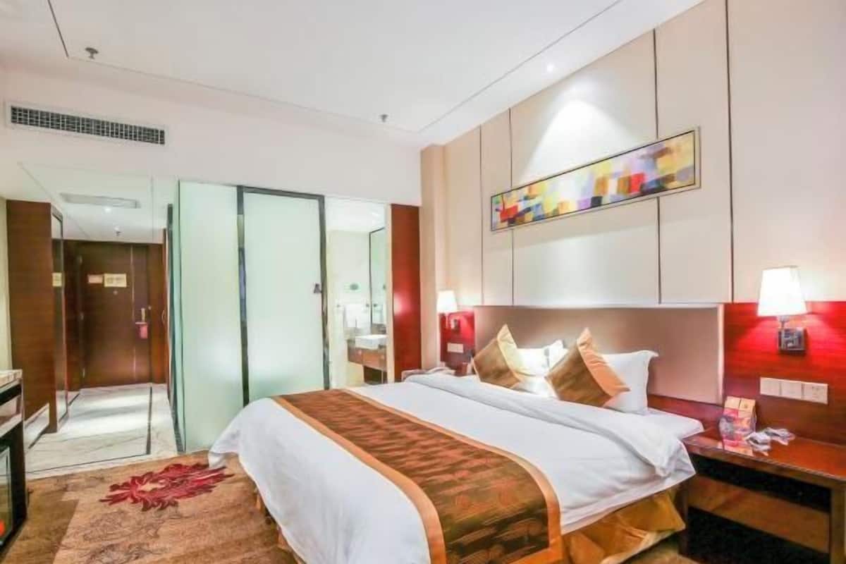 A hotel room with a bed, bedside tables, a mirror, a painting, and a red carpet.