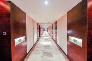 Un couloir d’hôtel avec des boiseries, des portes de chambres numérotées et un sol recouvert de moquette.