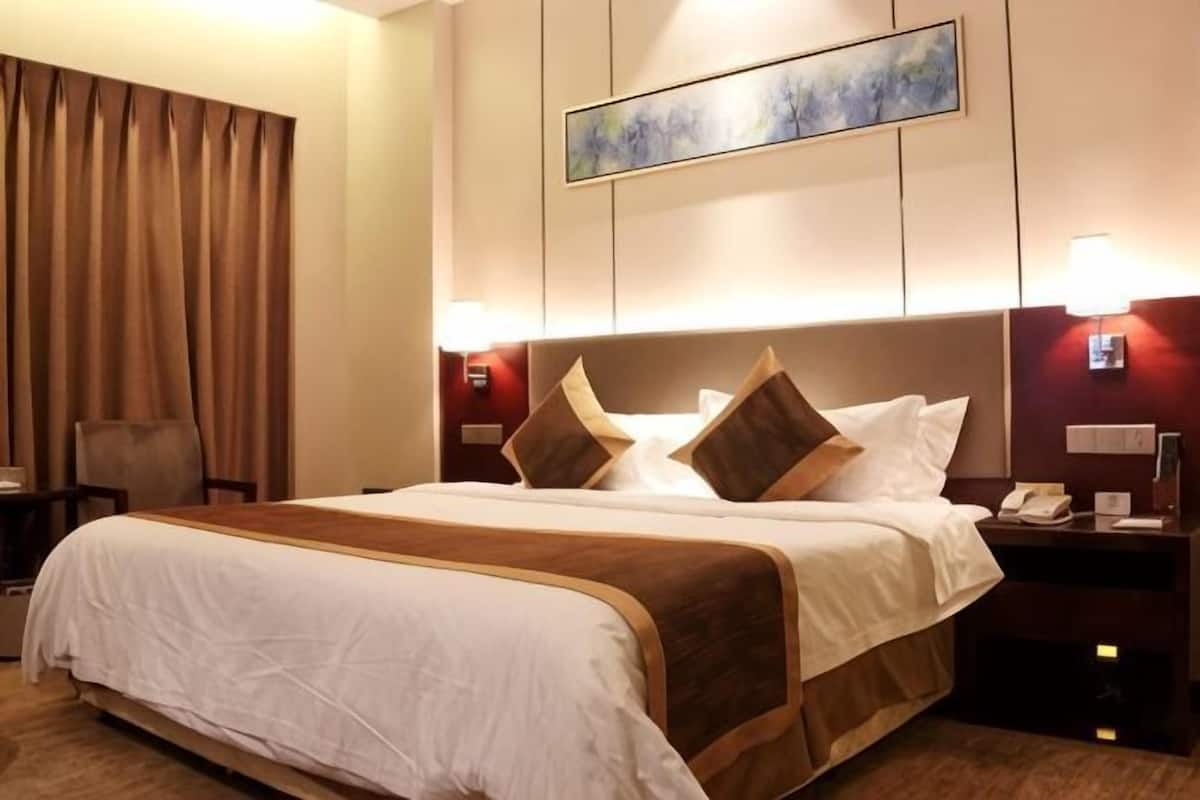 A hotel room with a large bed, a chair, a desk with a lamp, and a painting on the wall.