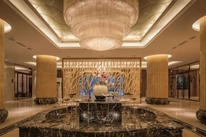 Un hall d’entrée spacieux, doté d’un comptoir de réception en marbre, d’un grand lustre et d’un mur décoratif agrémenté d’éléments verticaux.