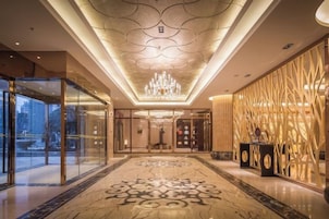 A hotel lobby with a chandelier, a patterned floor, and a reception desk.