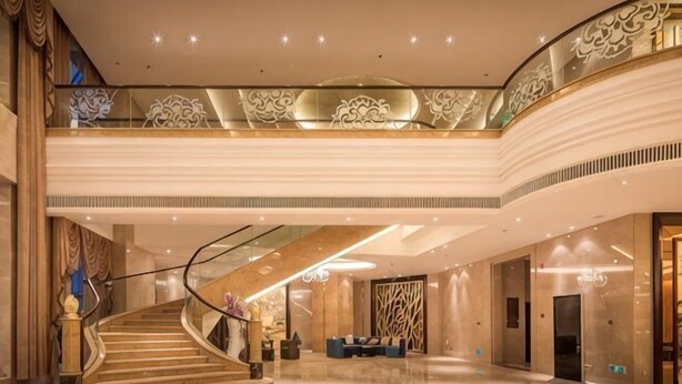Un vestíbulo amplio con una escalera monumental, un mostrador de recepción y un techo alto con iluminación decorativa.