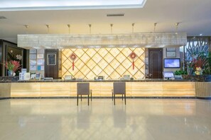 A hotel reception area with a reception desk, two chairs, a TV, and decorative plants. - Liuyiju International Hotel Yongfeng (Yongfeng)