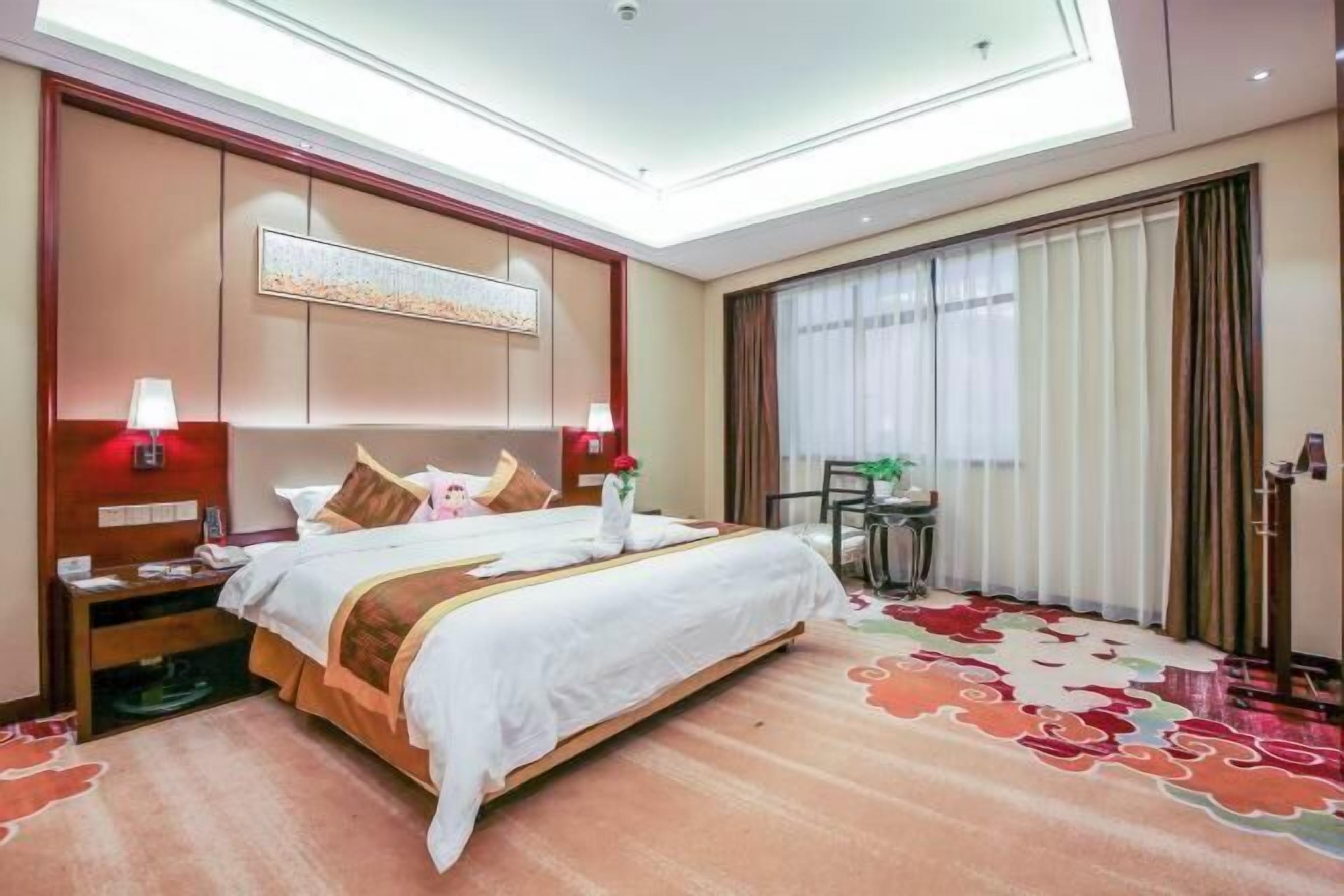 A hotel room with a large bed, bedside lamps, a desk, and a view of the outdoors through the window.