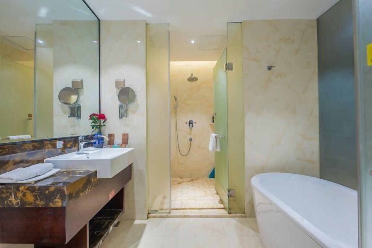 A modern bathroom with a marble vanity, a large mirror, a bathtub, and a glass-enclosed shower area.