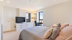 A bedroom with a bed, a TV on a dresser, a desk, and two windows. - Lovely Luminous 3 Bed Flat, With Secure Ev Parkng (London)