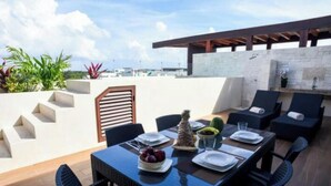 Un área de comedor al aire libre con una mesa lista para dos personas, rodeada de sillas, un muro de piedra y una estructura de pérgola.
