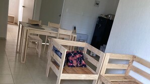 Huoneessa on useita vierekkäin aseteltuja puisia penkkejä, laattalattia ja taustalla ovi.