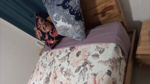 Sängyssä on kukkakuviollinen päiväpeite, koristeellinen koristetyyny ja puinen pääty.