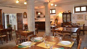 Un espace repas avec des tables et des chaises en bois, une cuisine à l’arrière-plan et des piliers en pierre.