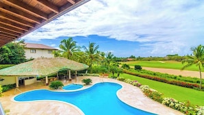 A swimming pool with a thatched roof structure, surrounded by a landscaped garden with palm trees and a golf course in the background. - "srvittinivillas Lmvll7/big Espacius View, Event Priv/ Villa  Resort" (La Romana)