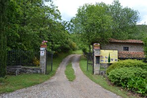 A gravel path leading to a stone building with a tiled roof, surrounded by greenery and a signboard.