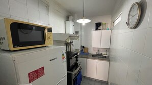 Eine kompakte Küche mit Mikrowelle, Kühlschrank, Backofen und einer Uhr an der Wand.