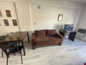 A living room with a brown sofa, a dining table with chairs, a TV, and a small desk.