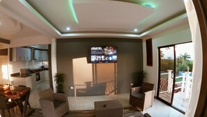 Ein modernes Wohnzimmer mit Flachbildfernseher, Korbmöbeln und Blick auf den Balkon.