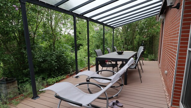 A covered patio with a table and chairs, surrounded by lush greenery.