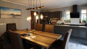 A modern kitchen with dark cabinets, a wooden dining table, and a hanging light fixture.