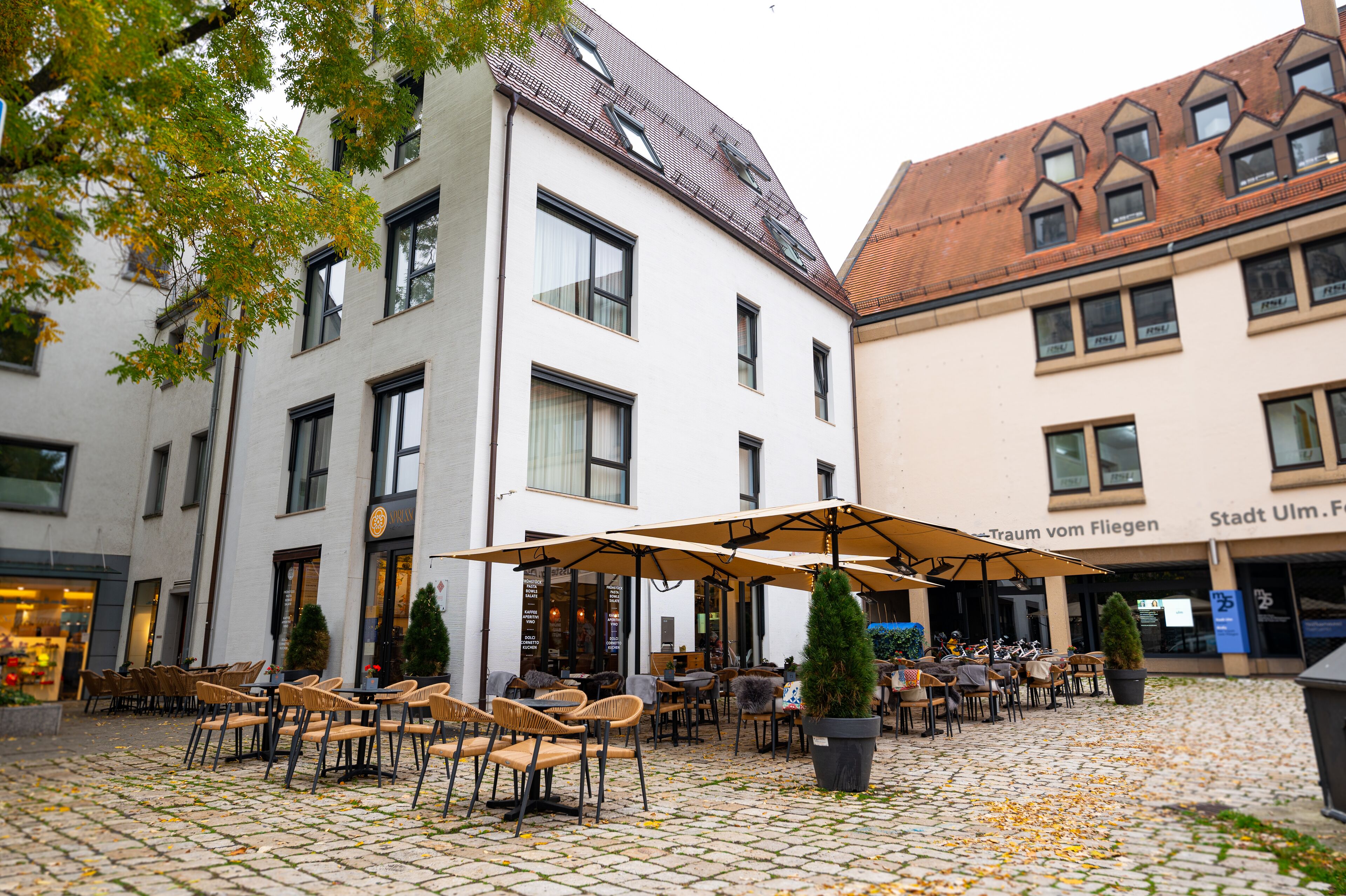 A courtyard with outdoor seating, a potted tree, and a building with a tiled roof.