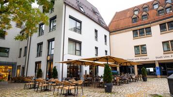 A courtyard with outdoor seating, a potted tree, and a building with a tiled roof.