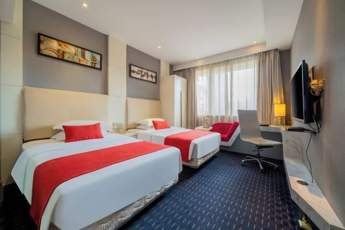 Ein Hotelzimmer mit drei Betten, einem Schreibtisch, einem Stuhl, einem Fernseher und Bildern an den Wänden.