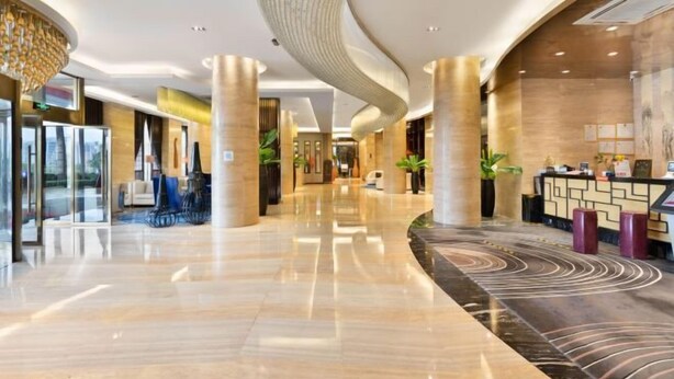 A modern hotel lobby with a curved ceiling, marble flooring, and a reception desk with a patterned design. - Shengzhan Hotel (Chongzuo)