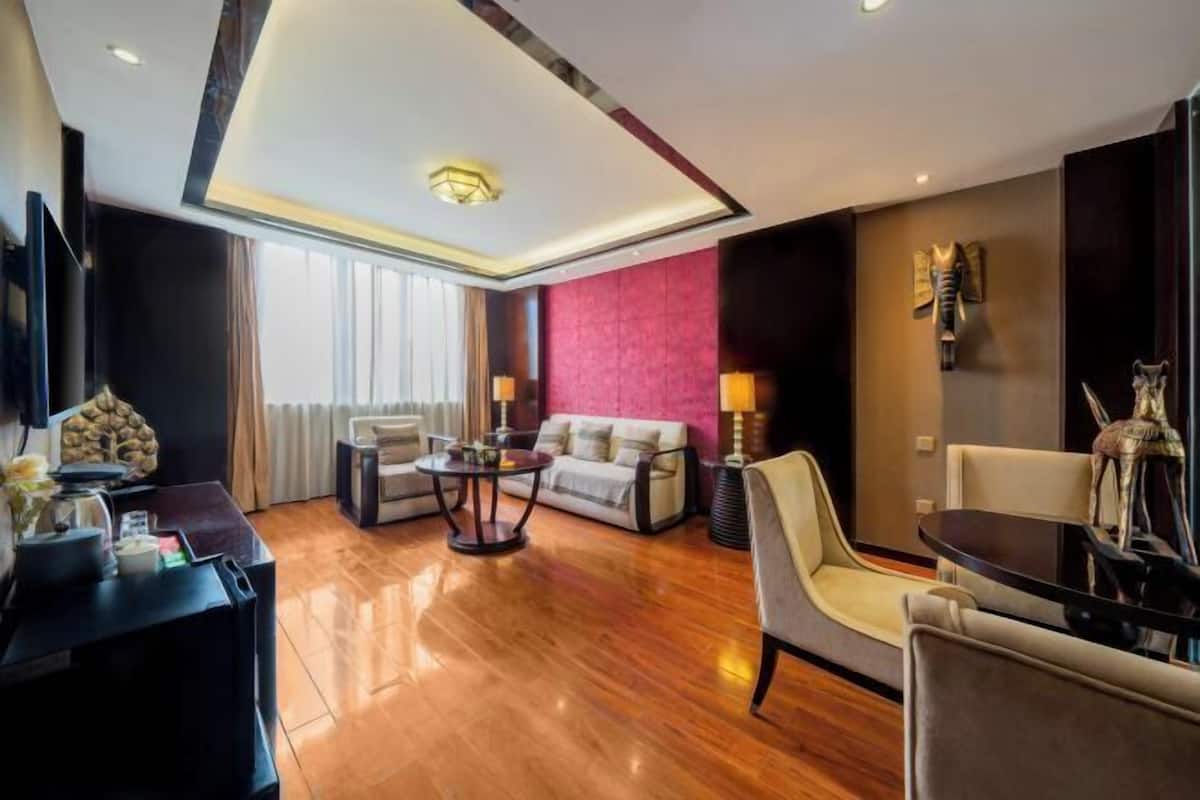 Ein modernes Hotelzimmer mit Holzboden, einer Couch, einem Sessel, einem kleinen Tisch und einem Fernseher.