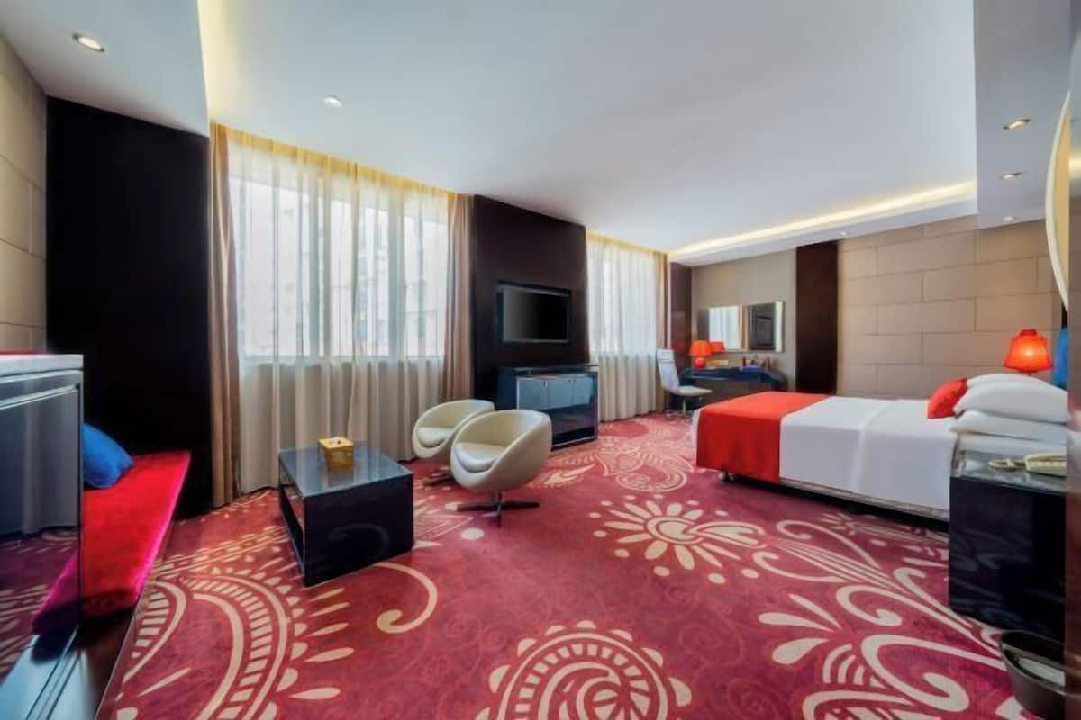 Ein Hotelzimmer mit Bett, Fernseher, Schreibtisch und einer Sitzecke mit Stühlen.