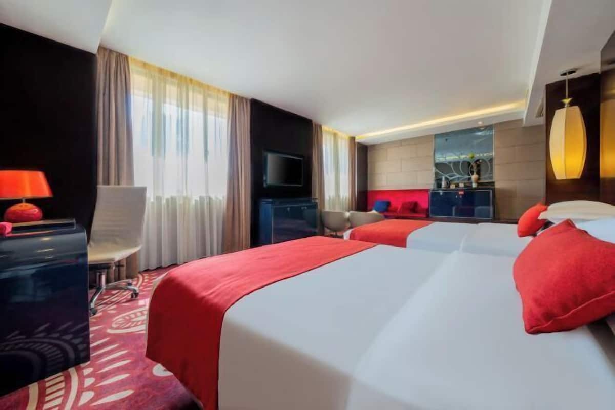 Ein Hotelzimmer mit zwei Betten, einem Schreibtisch, einem Fernseher und einer roten Akzentwand.