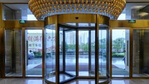 A revolving door with glass panels and a golden decorative element above it. - Shengzhan Hotel (Chongzuo)