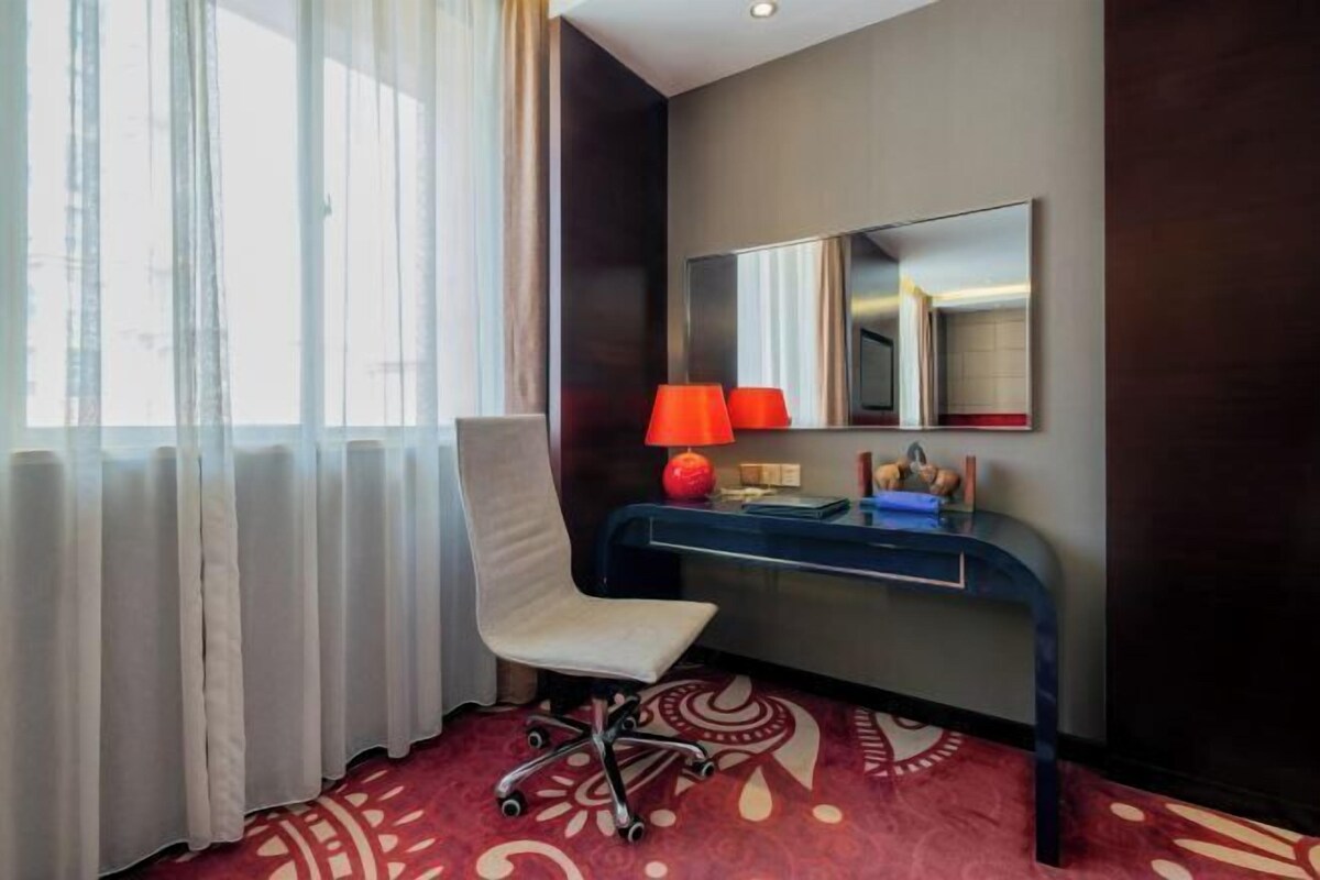 A hotel room with a desk, chair, and a large mirror.