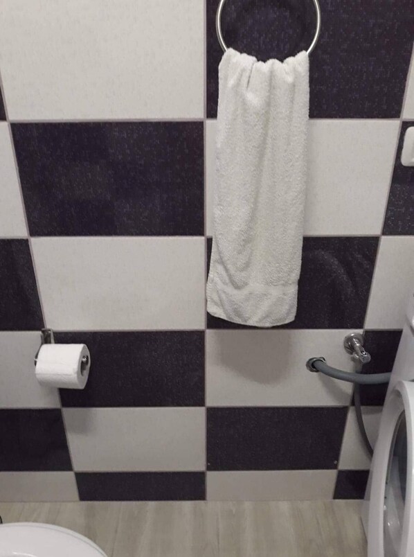 A bathroom with black and white checkered tiles, a white towel hanging on a metal ring, a toilet paper roll, and a hand dryer.
