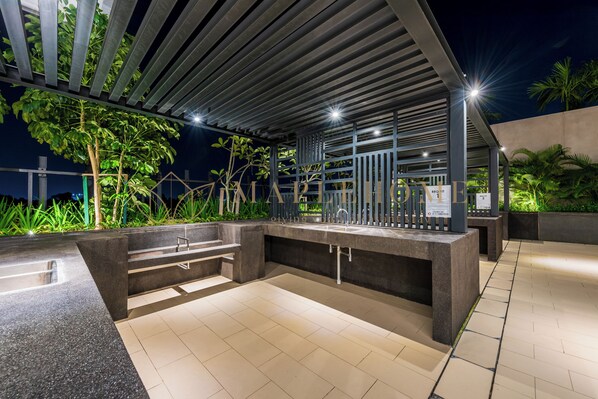 Un espace cuisine extérieur doté d’un évier encastré, d’un banc et d’une pergola au-dessus.