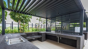 An outdoor kitchen area with a built-in sink, a barbecue pit, and a pergola structure.