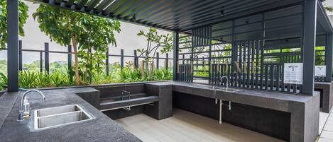 An outdoor kitchen area with a built-in sink, a barbecue pit, and a pergola structure.