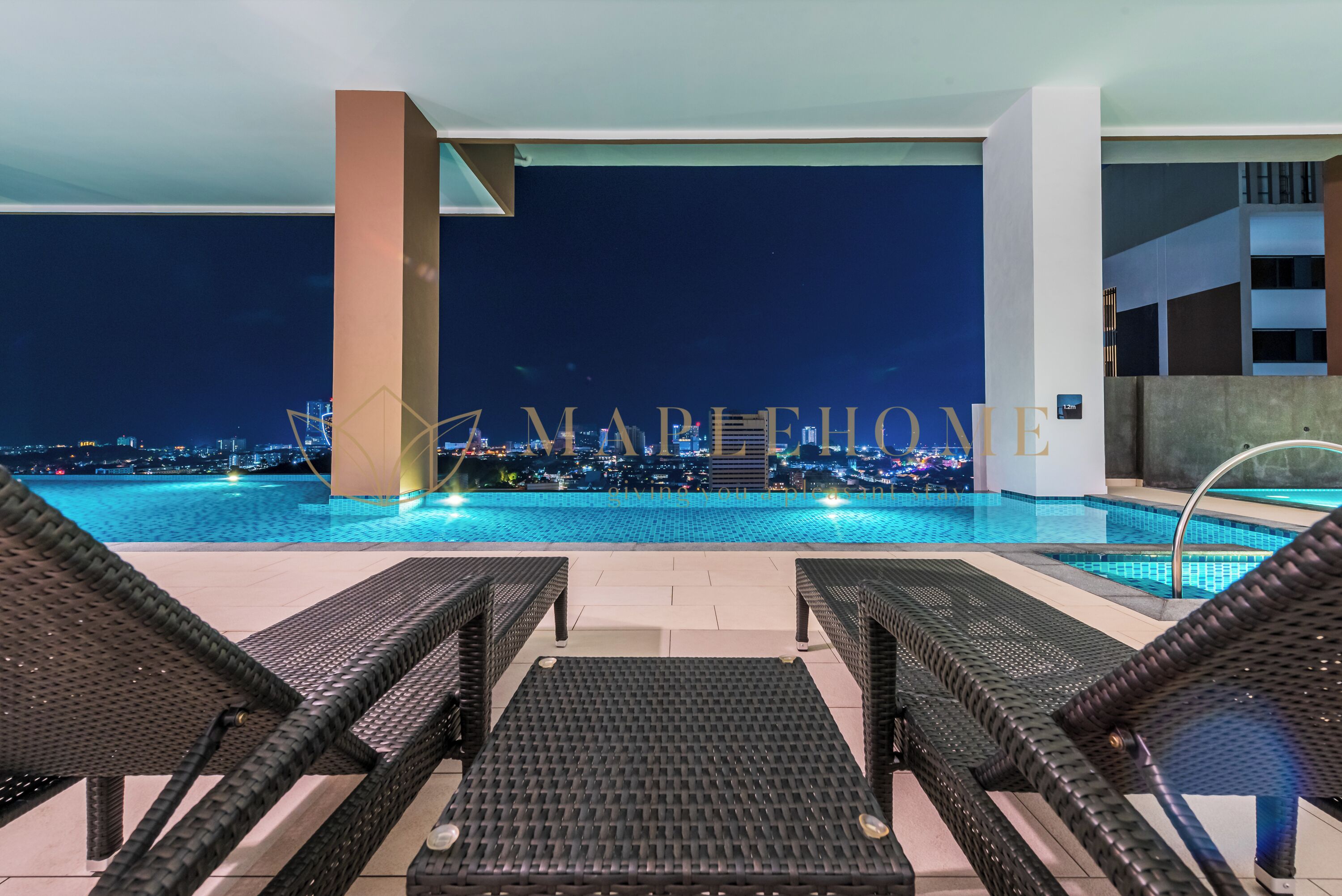 Vista nocturna de una piscina con sillones de descanso y un paisaje urbano al fondo.
