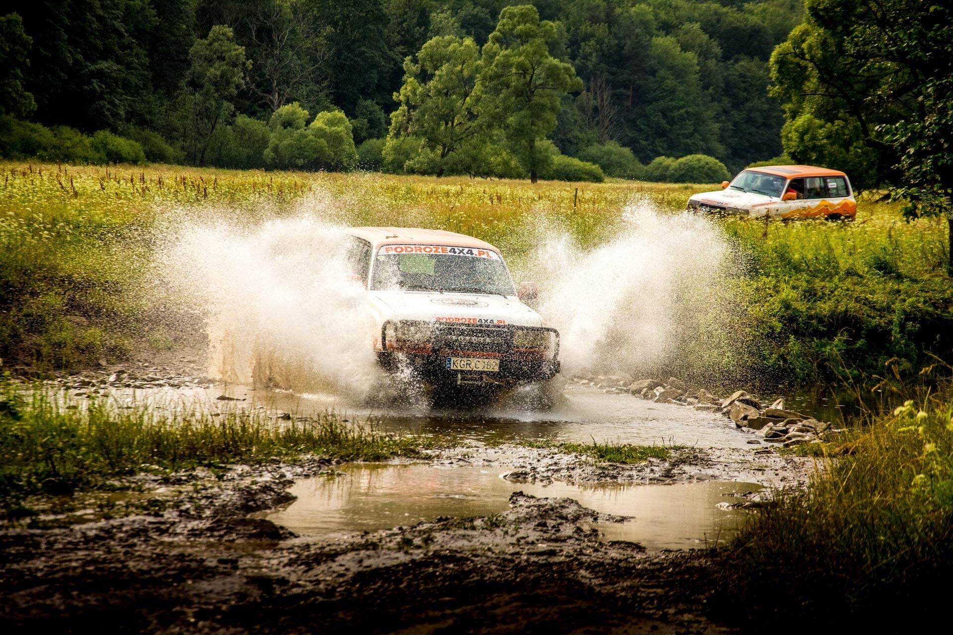 A vehicle driving through a muddy puddle, splashing water around.