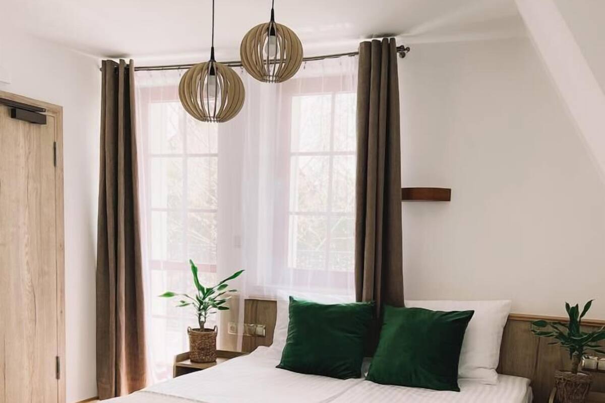 Ein Schlafzimmer mit einem großen Bett, zwei Pendelleuchten, einem Fenster mit Vorhängen und einem Holzboden.