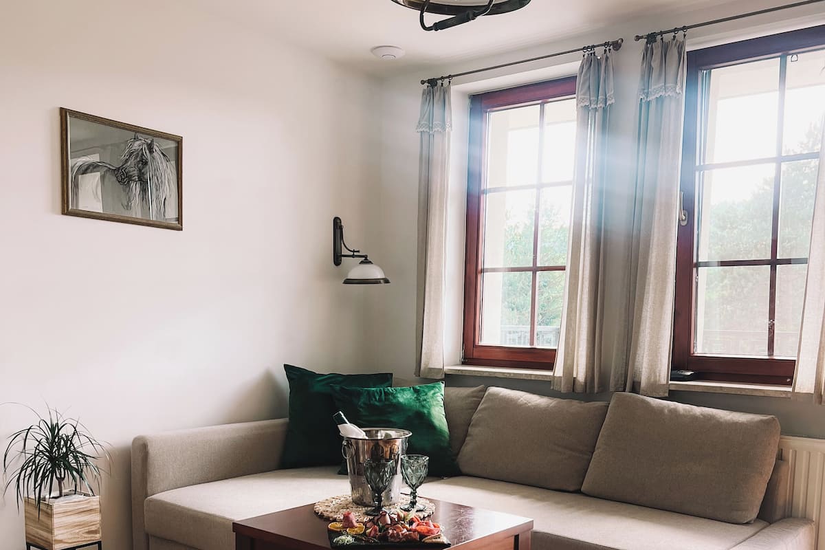 Ein Wohnzimmer mit einer Couch, einem Couchtisch, einem Gemälde und einem Fenster mit Vorhängen.