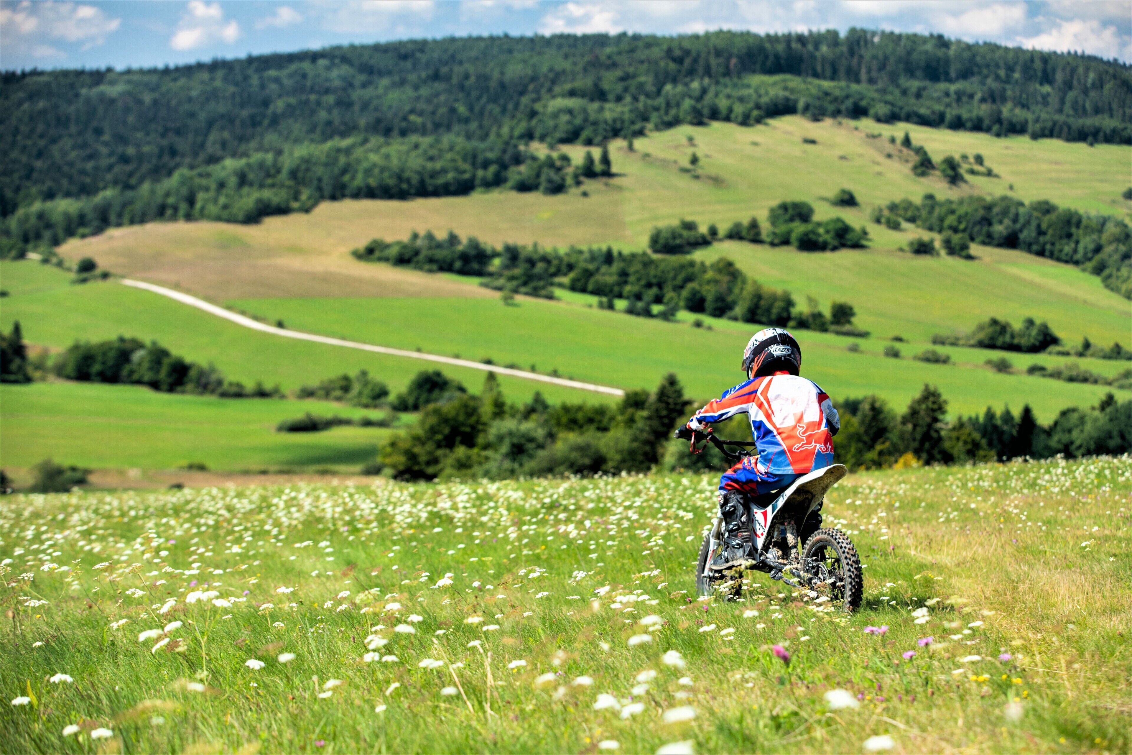 Een persoon die een motorfiets bestuurt in een grasveld, met een heuvelachtig landschap op de achtergrond.